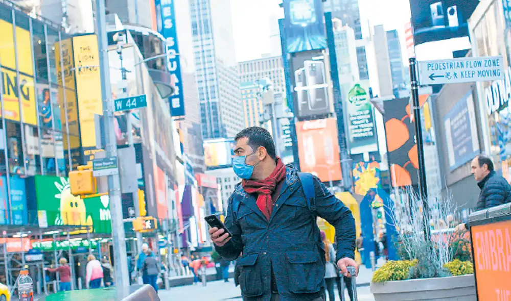 Precaución. Un hombre se protege con una mascarilla mientras lleva dos bolsas de víveres por el barrio de Queens.