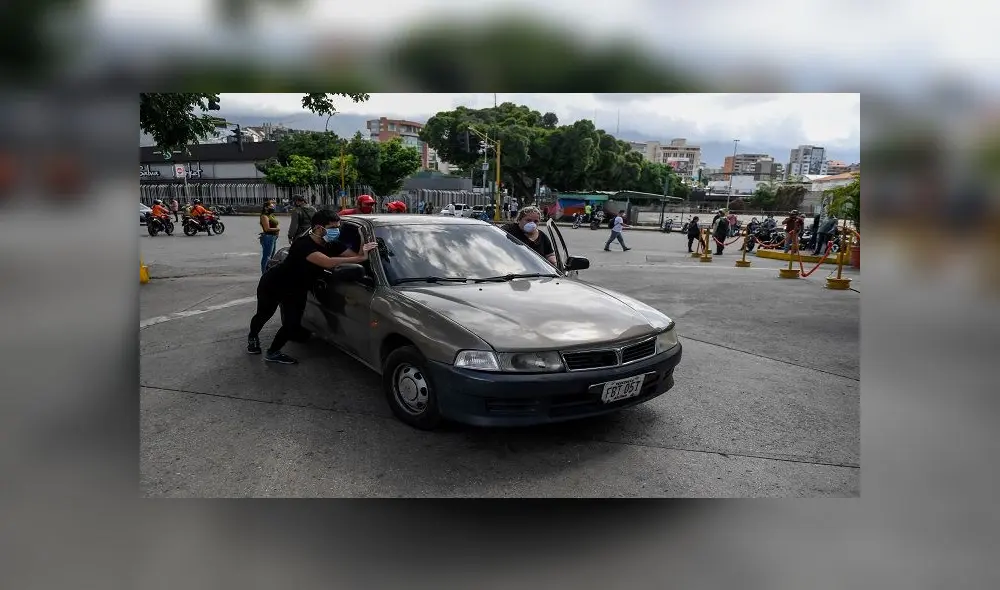 People push a car to refuel its tank near a gas station in Caracas on June 1, 2020 amid the novel coronavirus (COVID-19) outbreak. - Venezuela will increase fuel prices in June, President Nicolas Maduro said on Saturday, putting a limit on state subsidies that for decades had allowed citizens to fill their gas tanks virtually for free. (Photo by Federico PARRA / AFP)