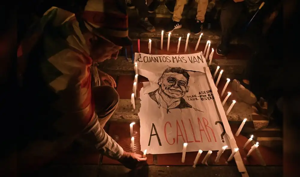 A man lights a candle around a poster reading "How many more are you going to silence?" and depicting Dilan Cruz, a young demonstrator who had been wounded by a member of the Mobile Anti-Disturbance Squadron (ESMAD) during a protest against the Colombian government and died yesterday, during a vigil in Cali, Colombia, on November 26, 2019. - Under-fire Colombian President Ivan Duque will meet with protest leaders on Tuesday, a minister announced, after five consecutive days of anti-government protests. The meeting will form part of the national dialogue Duque launched on Sunday to address corruption, economic inequality and other woes. (Photo by LUIS ROBAYO / AFP)