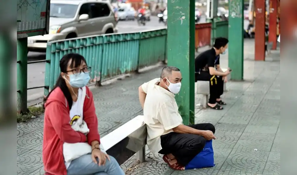 Ciudadanos con mascarillas protectoras esperan en una parada de autobús cuando regresan del trabajo en Hanoi. Foto: AFP.