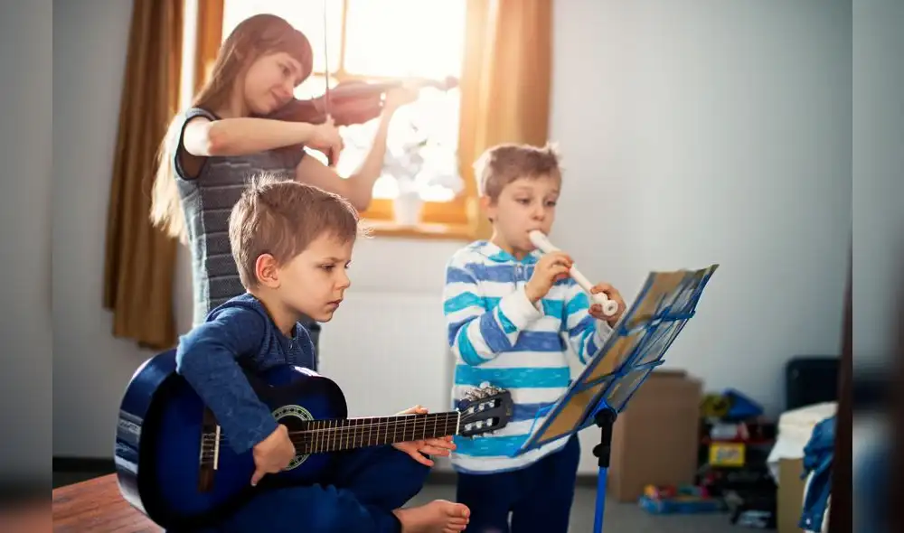 Sister and two brothers having fun playing music together. Sun is shining through the window. The girl is aged 10 and the boys are aged 6. Kids are playing a guitar, a violin and a flute. Sister and two brothers having fun playing music together. Sun is shining through the window. The girl is aged 10 and the boys are aged 6. Kids are playing a guitar, a violin and a flute.