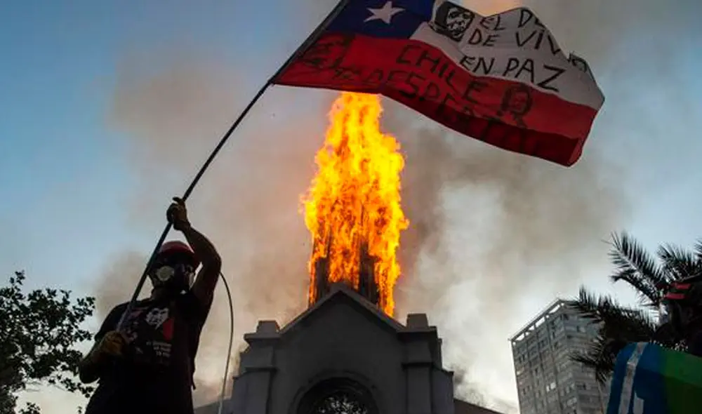 Un manifestante ondea una bandera de Chile frente a la Iglesia de la Asunción, que fue incendiada por encapuchados. Foto: AFP Un manifestante ondea una bandera de Chile frente a la Iglesia de la Asunción, que fue incendiada por encapuchados. Foto: AFP