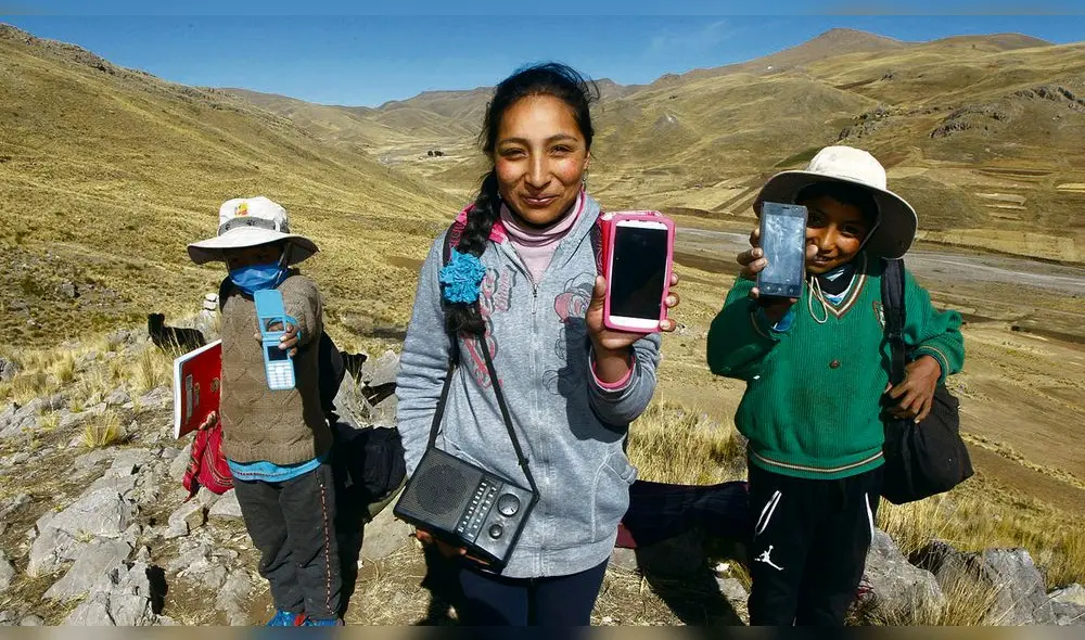 aprender en cerros. Estos tres hermanos muestran sus teléfonos para contactarse con sus maestros luego de la clase captada por radio.