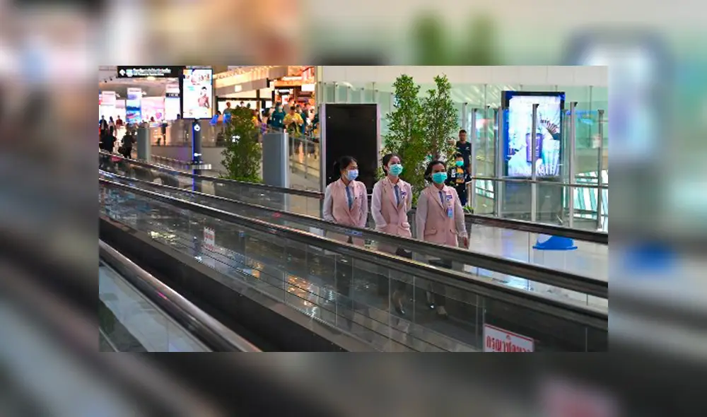 Empleados con máscaras protectoras viajan por una pasarela móvil en el aeropuerto de Suvarnabhumi en Bangkok. Foto: AFP.