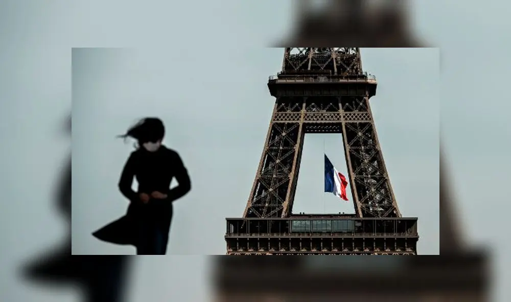 Una mujer con una mascarilla camina mientras una bandera nacional francesa ondea en la Torre Eiffel/Foto: Phillipe López/AFP.