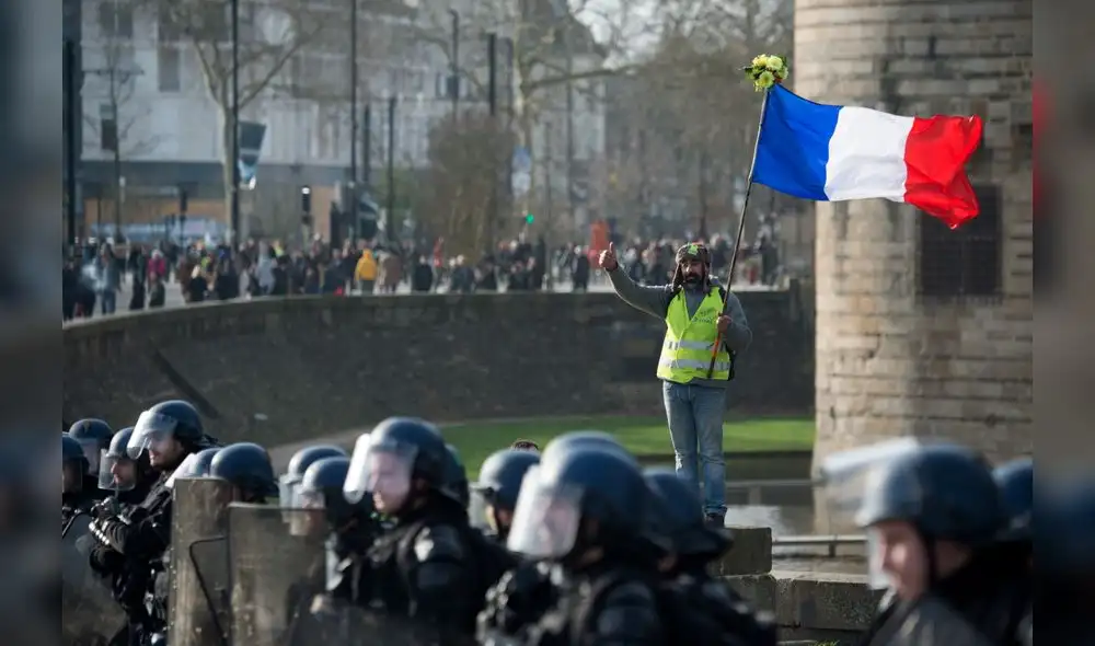 A demonstrator stands behind the police line as he hold the French flag during a protest called by the 'Yellow Vest' (gilets jaunes) anti-government movement as part of a nationwide multi-sector strike against the French government's pensions overhaul, on January 11, 2020 in Nantes, western France. - France's government on January 11, 2020, offered a possible compromise to unions waging a crippling, weeks-long transport strike against pension reform, offering to withdraw the most contested proposal that would in effect have raised the retirement age by two years. "To demonstrate my confidence in the social partners... I am willing to withdraw from the bill the short-term measure I had proposed" to set a so-called "pivot age" of 64 with effect from 2027, Prime Minister Edouard Philippe wrote in a letter to union leaders a day after they met seeking to end the labour action, now in its 38th day. (Photo by Loic VENANCE / AFP) A demonstrator stands behind the police line as he hold the French flag during a protest called by the 'Yellow Vest' (gilets jaunes) anti-government movement as part of a nationwide multi-sector strike against the French government's pensions overhaul, on January 11, 2020 in Nantes, western France. - France's government on January 11, 2020, offered a possible compromise to unions waging a crippling, weeks-long transport strike against pension reform, offering to withdraw the most contested proposal that would in effect have raised the retirement age by two years. "To demonstrate my confidence in the social partners... I am willing to withdraw from the bill the short-term measure I had proposed" to set a so-called "pivot age" of 64 with effect from 2027, Prime Minister Edouard Philippe wrote in a letter to union leaders a day after they met seeking to end the labour action, now in its 38th day. (Photo by Loic VENANCE / AFP)
