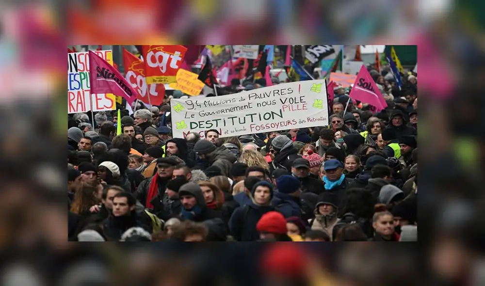 A demonstrator holds a sign reading "9,4 millions of poor, the government are looting us, dismissal"  during a demonstration against the pension overhauls, in Paris, on December 5, 2019, as part of a national general strike. - Trains cancelled, schools closed: France scrambled to make contingency plans on for a huge strike against pension overhauls that poses one of the biggest challenges yet to French President's sweeping reform drive (Photo by Alain JOCARD / AFP)