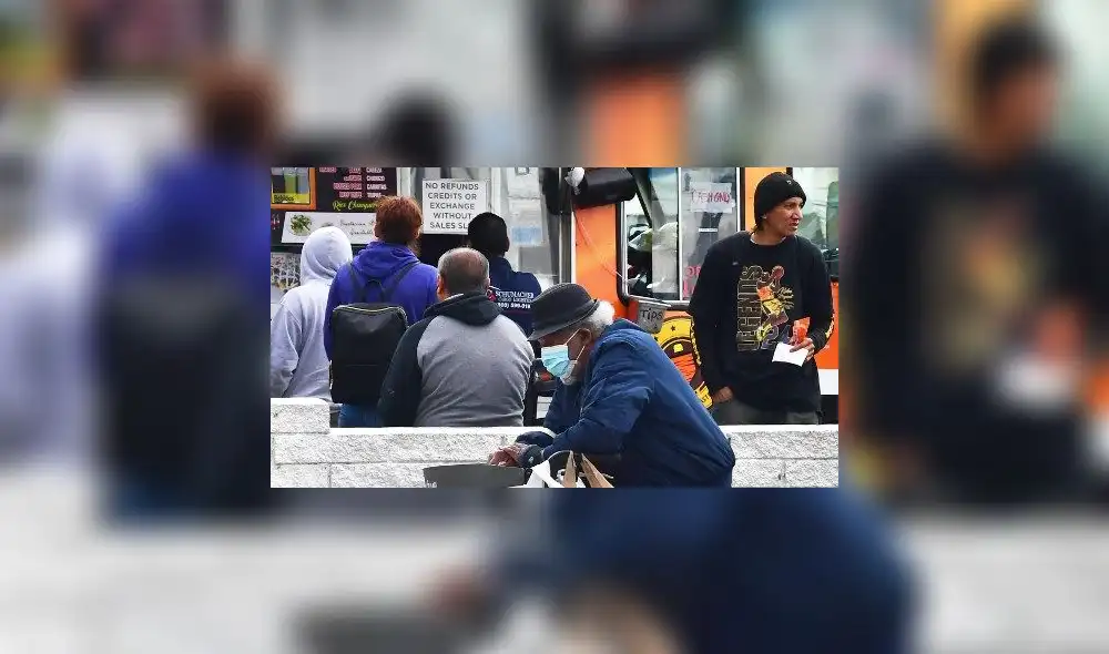 Un anciano con una mascarilla pasa junto a unas personas que esperaban en la fila de un Food Truck en Los Ángeles. Foto: AFP. Un anciano con una mascarilla pasa junto a unas personas que esperaban en la fila de un Food Truck en Los Ángeles. Foto: AFP.