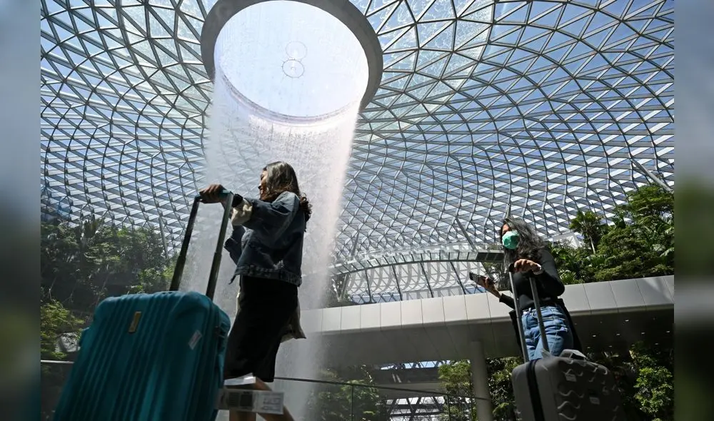 A traveller (R), wearing a protective facemask amid fears about the spread of the COVID-19 novel coronavirus, walks past the Rain Vortex display at Jewel Changi Airport in Singapore on February 27, 2020. (Photo by Roslan RAHMAN / AFP) A traveller (R), wearing a protective facemask amid fears about the spread of the COVID-19 novel coronavirus, walks past the Rain Vortex display at Jewel Changi Airport in Singapore on February 27, 2020. (Photo by Roslan RAHMAN / AFP)