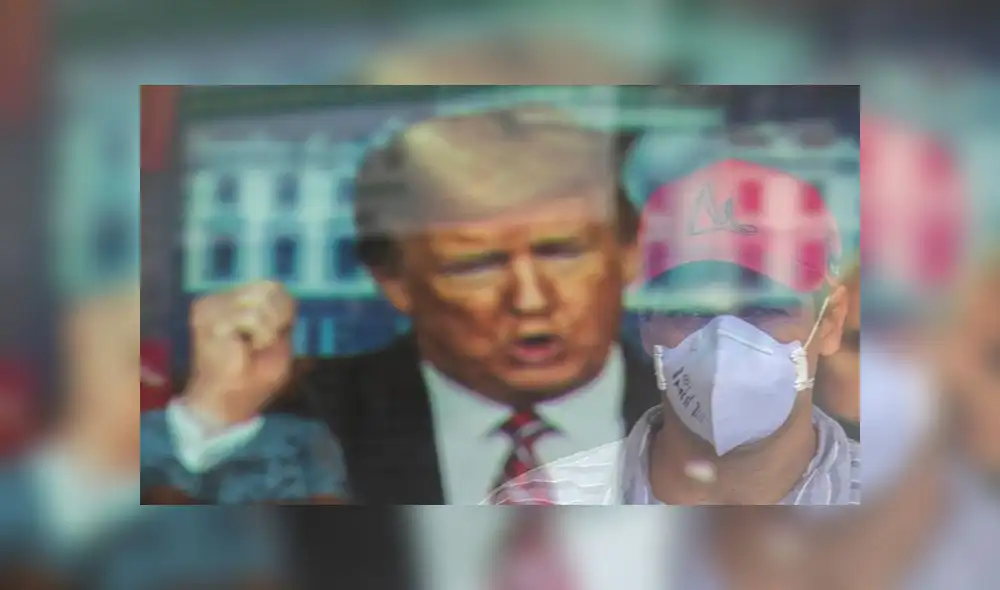 Un hombre con tapabocas aparece reflejado mientras observa un anuncio con el presidente estadounidense, Donald Trump, este lunes, en Brasilia (Brasil). Foto: EFE