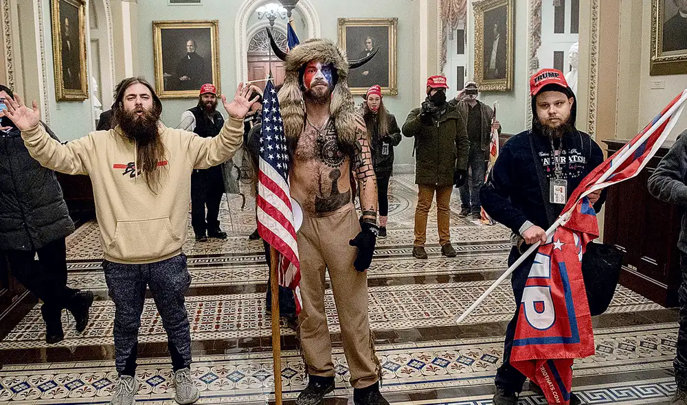 Se le busca. El del centro es Jake Angeli y se autodenomina "Yellowstone Wolf". Pertenece al grupo QAnon, que cree que hombres satánicos y pedófilos se oponen a Trump y están con los demócratas. Foto: AFP