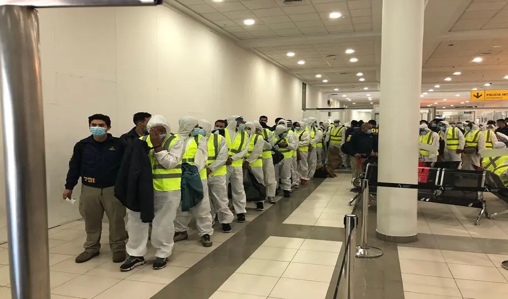 La PDI trasladó a los migrantes vestidos con overoles blancos con capucha, mascarillas, y esposados y acompañados cada uno por un agente. Foto: Ministerio del Interior y Seguridad Pública de Chile