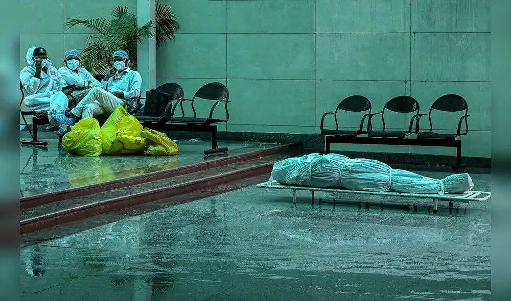 Trabajadores sanitarios en India se sientan junto al cadáver de una persona que murió como consecuencia de la Covid-19. Foto: AFP