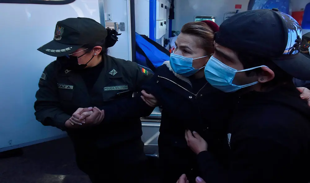 Jeanine Áñez (c) asistida la semana pasada por una policía y por su hijo José Armando Ribera (d) para bajar de una ambulancia que la llevó de vuelta a la prisión. Foto: EFE