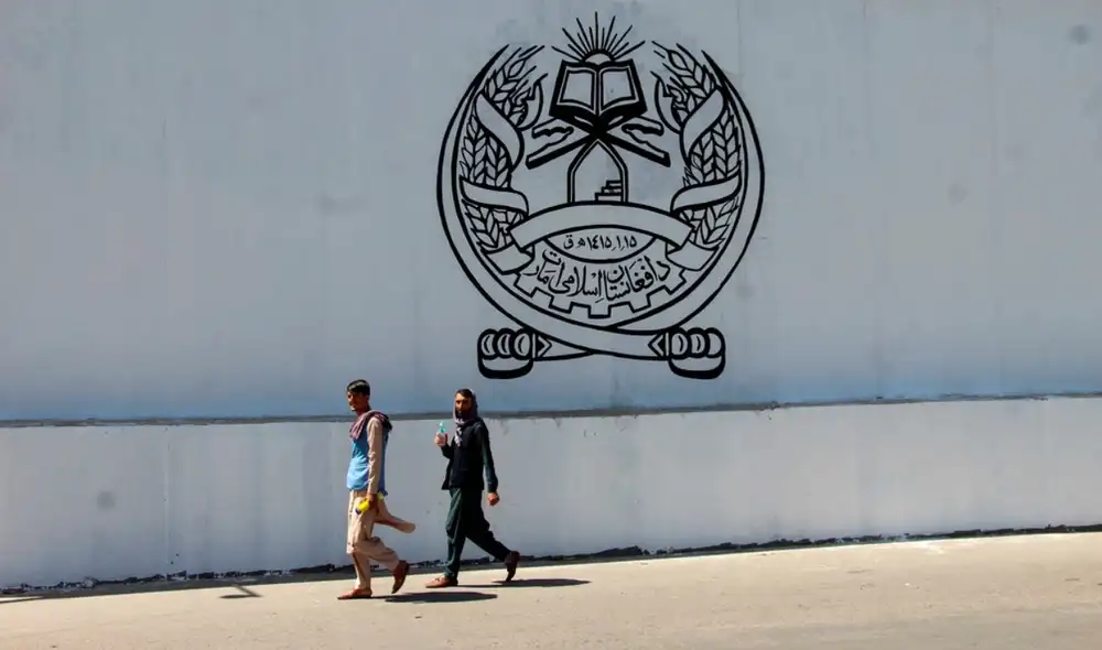 Afganos transitan al frente de la antigua embajada estadounidense, en cuya pared está el sello del gobierno talibán: Emirato Islámico de Afganistán. Foto: EFE