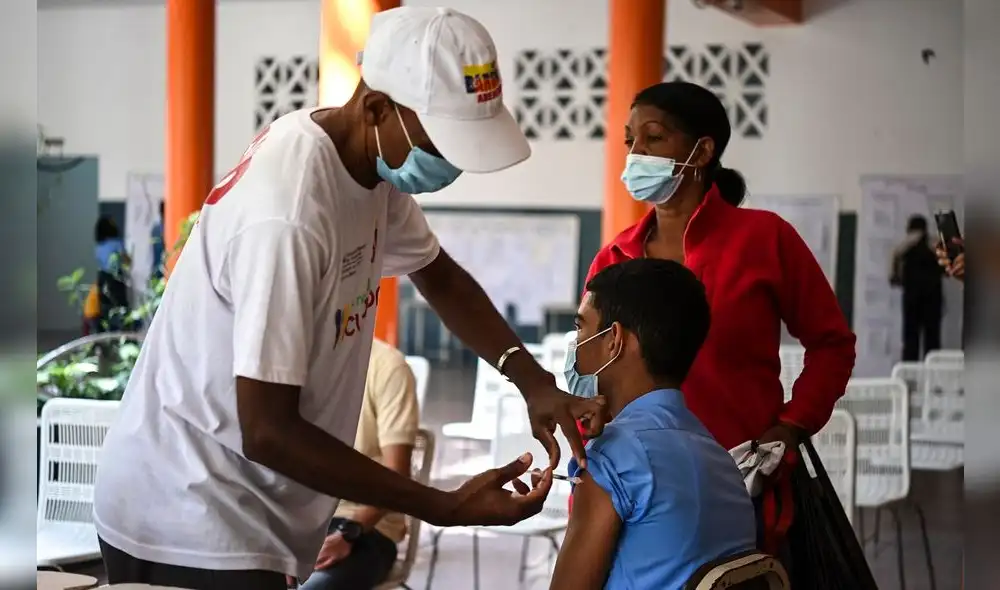 Un joven acompañado por su madre está siendo inoculado con Vero Cell, una vacuna contra la COVID-19. Foto: AFP