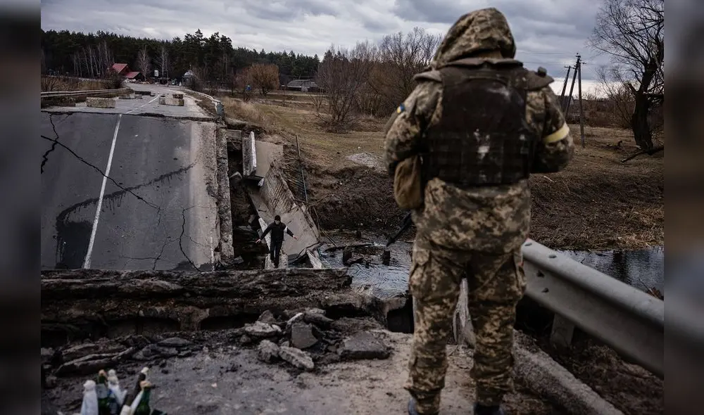 Un militar ucraniano mira a un civil cruzando un puente volado en una aldea, al este de la ciudad de Brovary, el 6 de marzo de 2022. Foto: AFP