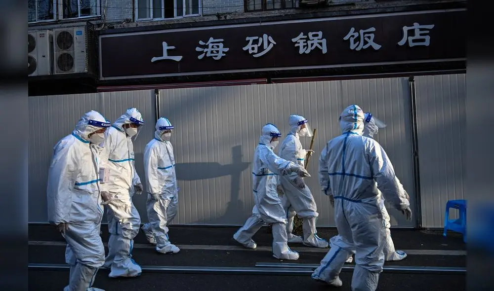 Los trabajadores laboran con ropa protectora en un área donde se están colocando barreras para cerrar las calles alrededor de algunas áreas de confinamiento. Foto: AFP