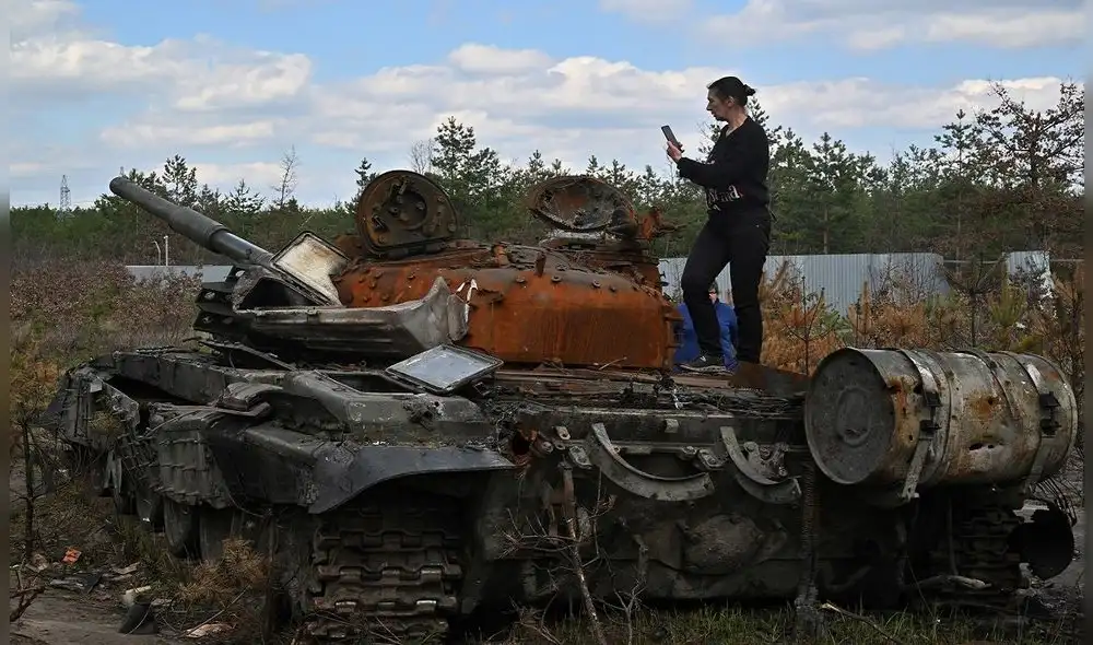 Una mujer toma una fotografía mientras se encuentra en un tanque ruso destruido en la aldea de Dmytrivka, región de Kiev. Foto: AFP