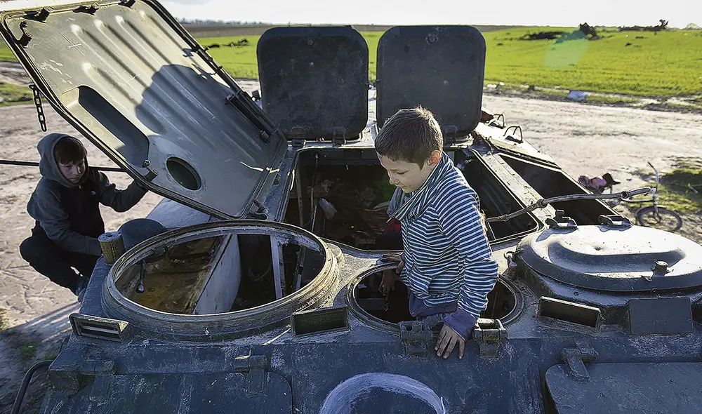 Juguemos a la guerra. Niños ucranianos juegan en los escombros de un tanque ruso. Foto: