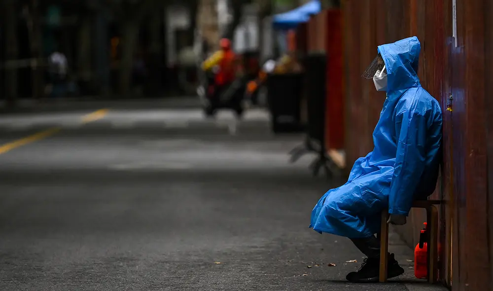 Un trabajador se sienta junto a una valla erigida para cerrar una zona residencial bajo encierro de COVID-19 en Shanghái. Foto: AFP