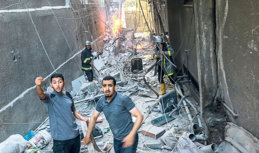 Bombardeos. Jóvenes palestinos evacúan un edificio que fue impactado por misiles israelíes. Foto: EFE