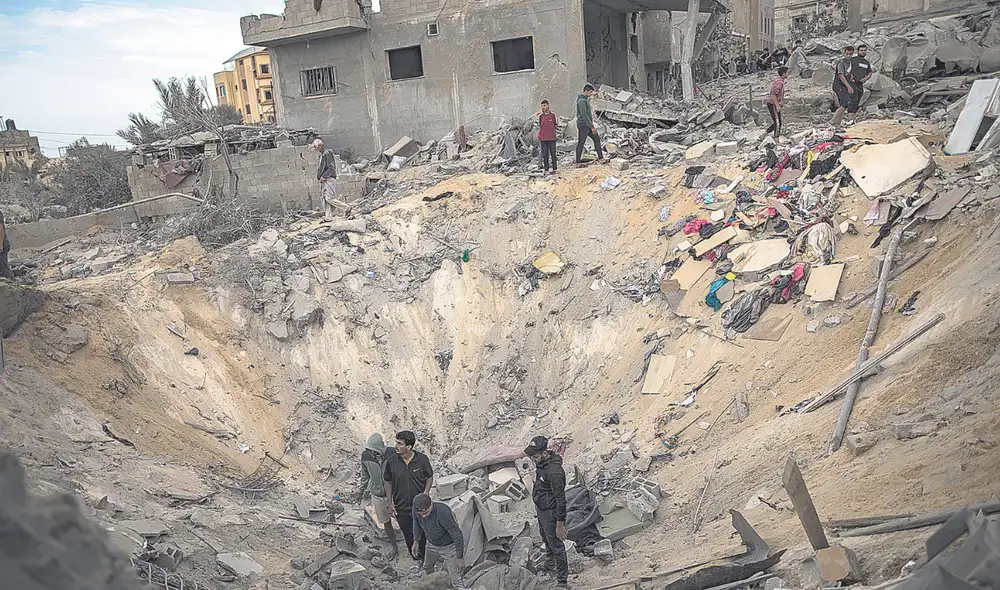 Bombardeo. Vecinos buscan restos humanos en el cráter dejado por la explosión de un misil que derrumbó un edificio en Gaza. Foto: EFE