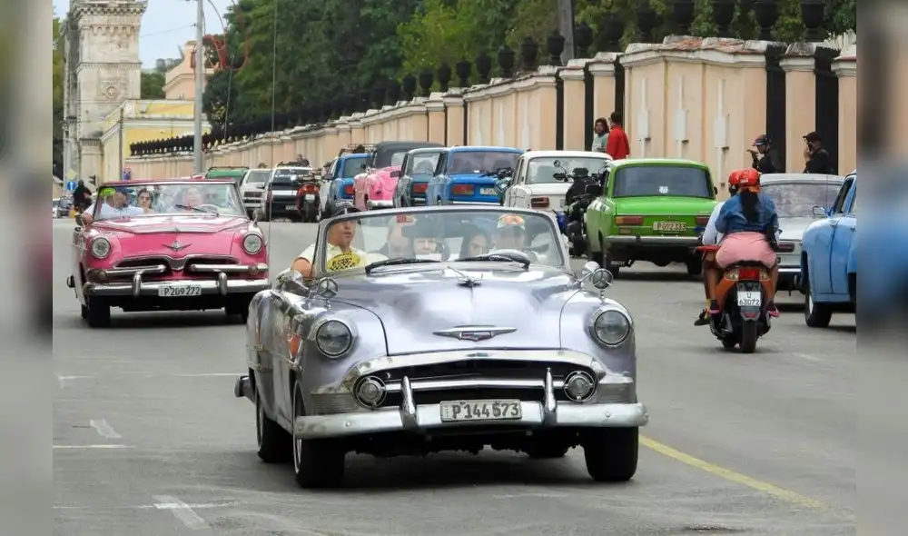 Turistas viajan en autos estadounidenses clásicos. Al lado, larga cola de vehículos para una gasolinera en La Habana. Foto: AFP