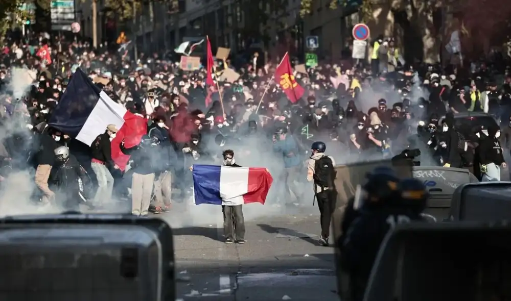 Manifestantes portan banderas nacionales francesas mientras se enfrentan a agentes del Cuerpo Republicano de Seguridad Francés.