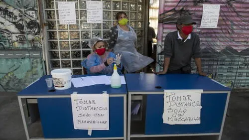 Volunteers wait, next to signs reading �Keep distance. Only with face masks�, for residents to come and take away lunches at a soup kitchen in La Pintana neighborhood, Santiago, on May 25, 2020, amid the new coronavirus pandemic. - Chile began Friday the delivery of 2.5 million boxes of basic products for the most vulnerable families amid protests due to food and job shortages caused by the measures imposed by the government against the new coronavirus pandemic. (Photo by MARTIN BERNETTI / AFP) La cuarentena total en algunas comunas de Santiago se extenderá hasta el 5 de junio. Foto: AFP.