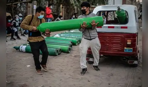 Dos hombres cargan un tanque de oxígeno vacío cuando llegan a la cola para recargarlo en Villa El Salvador, sur de Lima. Foto: Ernesto Benavides/AFP