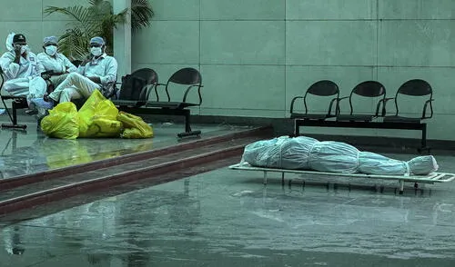 Trabajadores sanitarios en India se sientan junto al cadáver de una persona que murió como consecuencia de la Covid-19. Foto: AFP