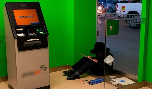 El niño está sentado sobre el piso realizando su tarea, mientras su madre trabaja como vendedora ambulante.