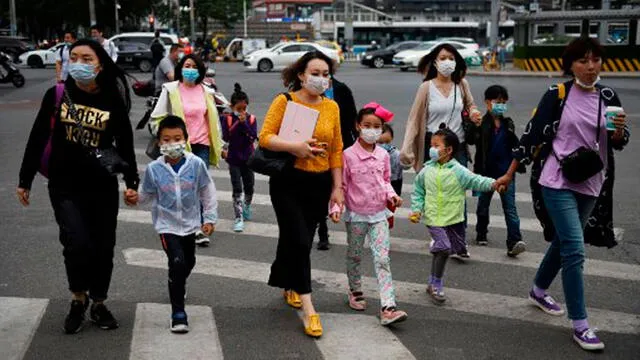 Un grupo de mujeres y niños usan mascarillas como precaución contra el coronavirus COVID-19 cuando cruzan una carretera en Beijing. Foto: AFP.