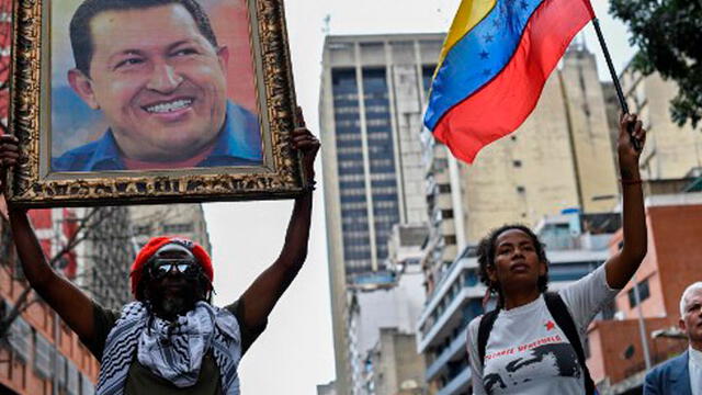 Mujer carga cuadra del expresidente de Venezuela, Hugo Chávez, en marcha a favor del oficialismo. Foto: AFP.