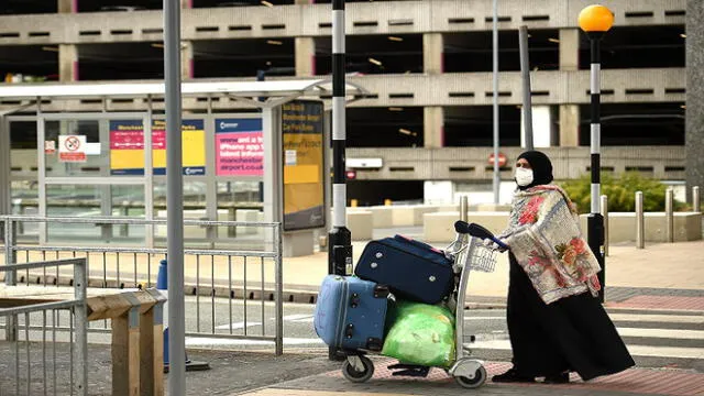 A passenger wearing PPE (personal protective equipment), including a face mask as a precautionary measure against COVID-19, pushes his luggage after arriving at Manchester Airport in northern England, on June 8, 2020, as the UK government's planned 14-day quarantine for international arrivals to limit the spread of the novel coronavirus begins. (Photo by Oli SCARFF / AFP)