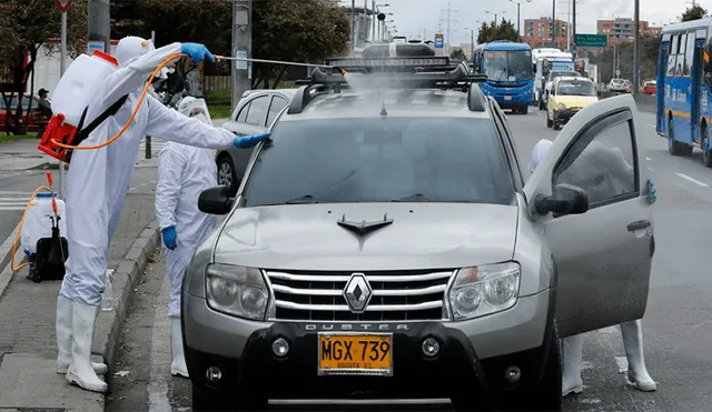 Vestidos con traje antifluido y equipados con contenedores de fumigación desinfectan todo tipo de vehículos.