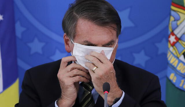 (FILES) In this file photo taken on March 18, 2020 Brazilian President Jair Bolsonaro covers his face with a face mask during a press conference regarding the COVID-19, coronavirus pandemic at the Planalto Palace, Brasilia. - Bolsonaro has very randomly complied with a decree in force in the Federal District of Brasilia that imposes the use of face masks "in all public places", amid the new coronavirus pandemic. Brazilian judge Renato Borelli decided on June 22, 2020 that a fine of 2,000 reais (around 340 euros) would be imposed on the head of state if he appeared again in public without a protective mask. (Photo by Sergio LIMA / AFP)