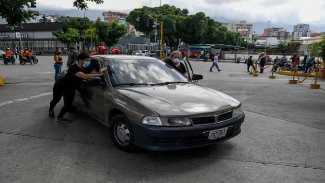 People push a car to refuel its tank near a gas station in Caracas on June 1, 2020 amid the novel coronavirus (COVID-19) outbreak. - Venezuela will increase fuel prices in June, President Nicolas Maduro said on Saturday, putting a limit on state subsidies that for decades had allowed citizens to fill their gas tanks virtually for free. (Photo by Federico PARRA / AFP)