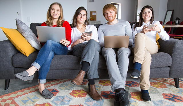 Group of freelance colleagues working at home. Four young people sitting on couch together and using gadgets. Freelance or home office concept