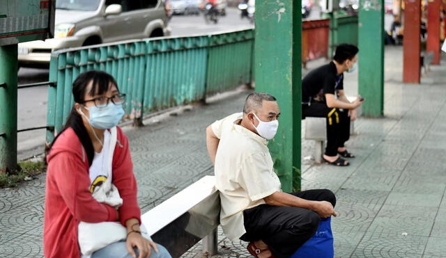Ciudadanos con mascarillas protectoras esperan en una parada de autobús cuando regresan del trabajo en Hanoi. Foto: AFP.