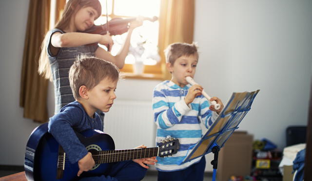 Sister and two brothers having fun playing music together. Sun is shining through the window. The girl is aged 10 and the boys are aged 6. Kids are playing a guitar, a violin and a flute.