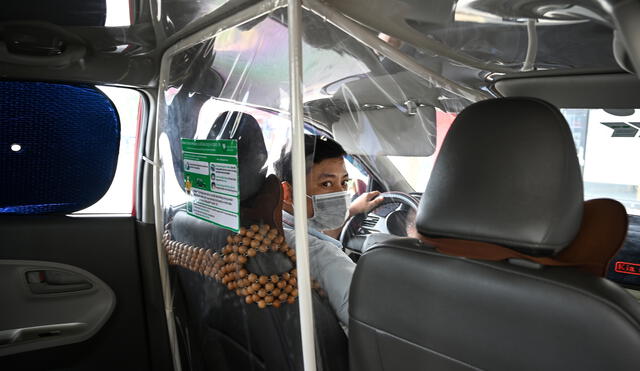 A taxi driver wearing a face mask looks on from behind a plastic screen as a preventive measure against the spread of COVID-19 novel coronavirus, in Hanoi on May 19, 2020. (Photo by Manan VATSYAYANA / AFP)