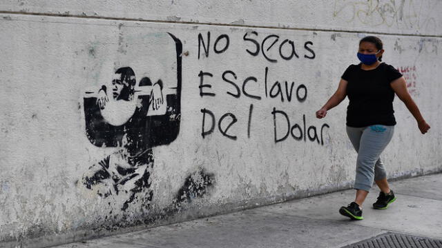 A woman wearing a face mask walks next to a graffiti reading �Don't be a slave of the dollar� in Caracas on April 27, 2020. - The minimum income of Venezuela will increase 77.7% from May 1, Labor Day, the government of Nicolas Maduro announced, but it will barely equal 4.6 dollars a month in a country hit by hyperinflation and a constant depreciation of the coin. (Photo by Federico PARRA / AFP)