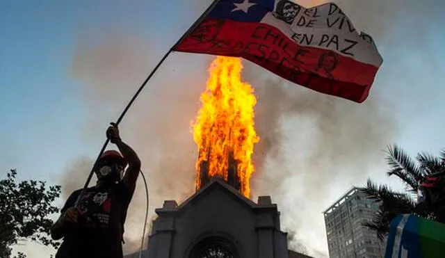 Un manifestante ondea una bandera de Chile frente a la Iglesia de la Asunción, que fue incendiada por encapuchados. Foto: AFP