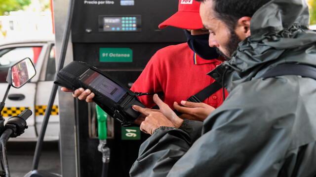 An employee wearing a protective face mask charges a costumer using the new biometric system for gasoline at a gas station in Caracas on June 1, 2020 amid the Covid-19 coronavirus pandemic. - Venezuela will increase fuel prices in June, President Nicolas Maduro said on Saturday, putting a limit on state subsidies that for decades had allowed citizens to fill their gas tanks virtually for free. (Photo by Federico PARRA / AFP)