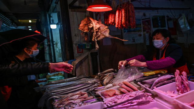 Customers buy food from a vendor (R) at a meat stall in Wuhan in China's central Hubei province on April 18, 2020. (Photo by Hector RETAMAL / AFP)