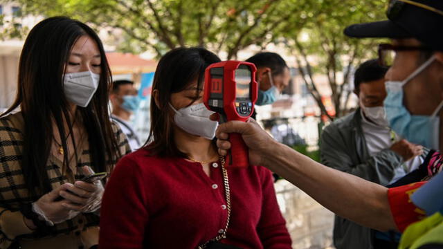 A worker wearing a face mask checks passengers body temperatures and a health code on their phones before they take a taxi after arriving at Hankou railway station in Wuhan, China's central Hubei province on May 12, 2020. - China reported no new domestic coronavirus infections on May 12, after two consecutive days of double-digit increases, including a new cluster over the weekend in Wuhan, which fuelled fears of a second wave of infections. (Photo by Hector RETAMAL / AFP)
