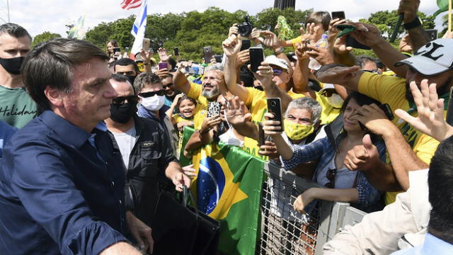 Brazil's President Jair Bolsonaro greets supporters upon arrival at Planalto Palace in Brasilia, on May 24, 2020, amid the COVID-19 coronavirus pandemic. - Despite positive signs elsewhere, the disease continued its surge in large parts of South America, with the death toll in Brazil passing 22,000 and infections topping 347,000, the world's second-highest caseload. (Photo by EVARISTO SA / AFP)