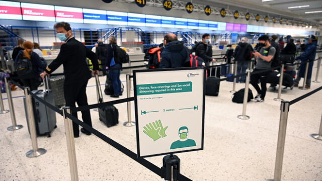 Passengers wearing PPE (personal protective equipment), including a face mask as a precautionary measure against COVID-19, socially distance as they queue at a check-in desk at Manchester Airport in northern England, on June 8, 2020, as the UK government's planned 14-day quarantine for international arrivals to limit the spread of the novel coronavirus begins. (Photo by Oli SCARFF / AFP)